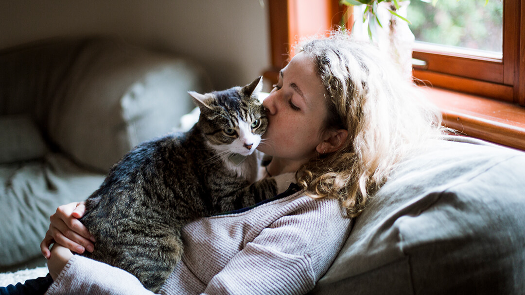 Mujer besando a su gato en la mejilla
