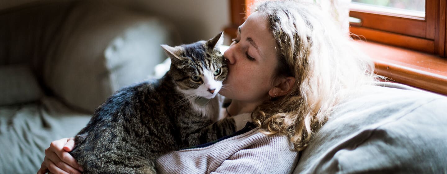Mujer besando a su gato en la mejilla