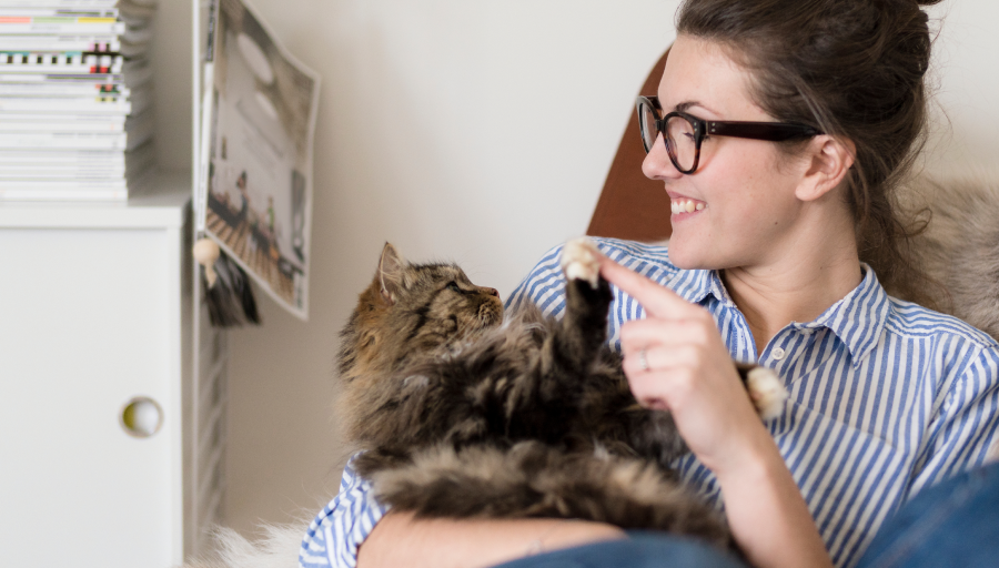 Una mujer sentada con su gato en su regazo tocando su pata con su dedo