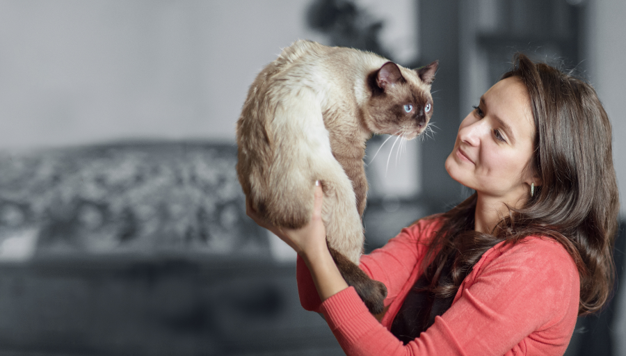 Una mujer mirando la cara de su gato mientras lo sostiene en el aire