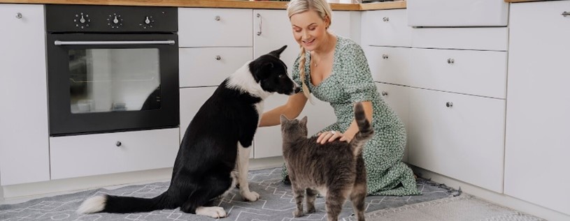 Mujer interactuando con un perro y un gato en la cocina de casa
