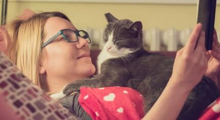 Mujer joven leyendo un libro con su gato por la noche