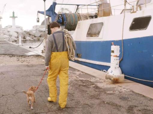 pescador paseando a su perro junto a un barco de pesca