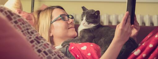 young woman reading a book with her cat at night